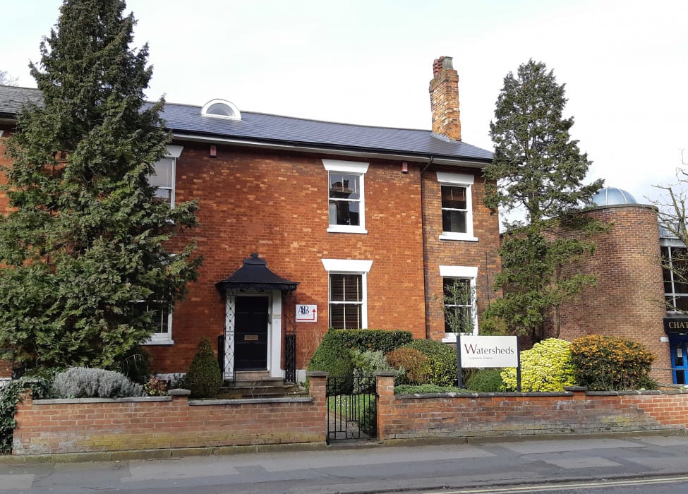 Brown face brick two storey  cottage, with two tall lush trees