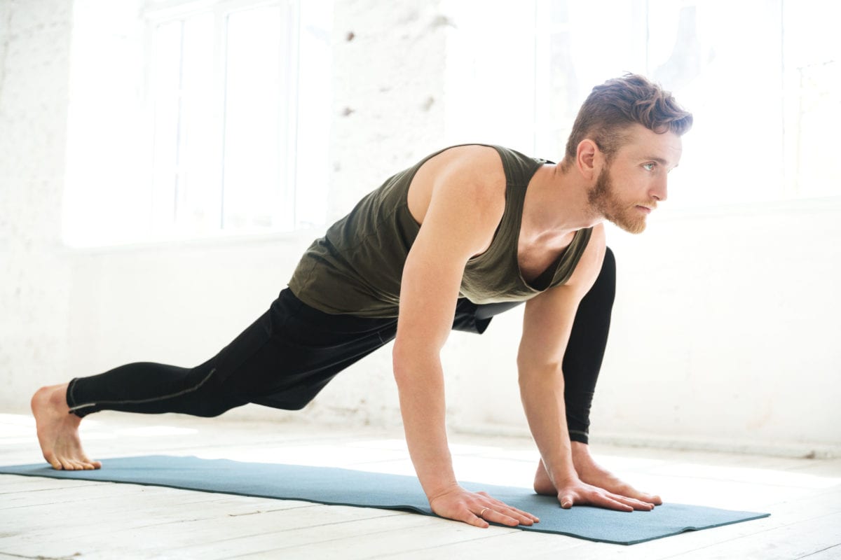 Handsome concentrated man doing yoga on mat
